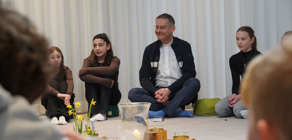 „Raum der Stille“: Im Schneidersitz reiht sich der Pallottinerpater zwischen den Sechstklässlern ein, die gemeinsam mit ihrer Klassenlehrerin Jennifer Schümann zentrale Erzählungen des Alten und Neuen Testaments erarbeiten.