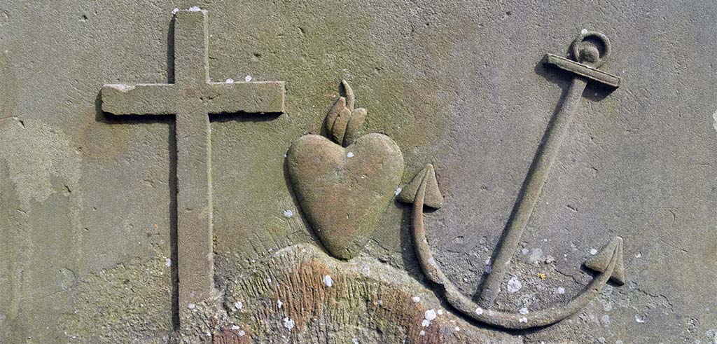 Christliche Symbole Kreuz, flammendes Herz und Anker herausgehoben in einer Steinplatte.