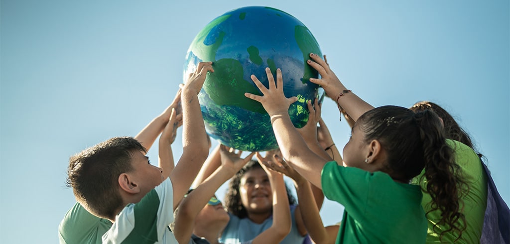 Kinder die gemeinsam im Freien den Erdplaneten halten Kinder die gemeinsam im Freien den Erdplaneten halten